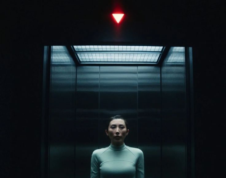 A figure in an elevator under a red signal
